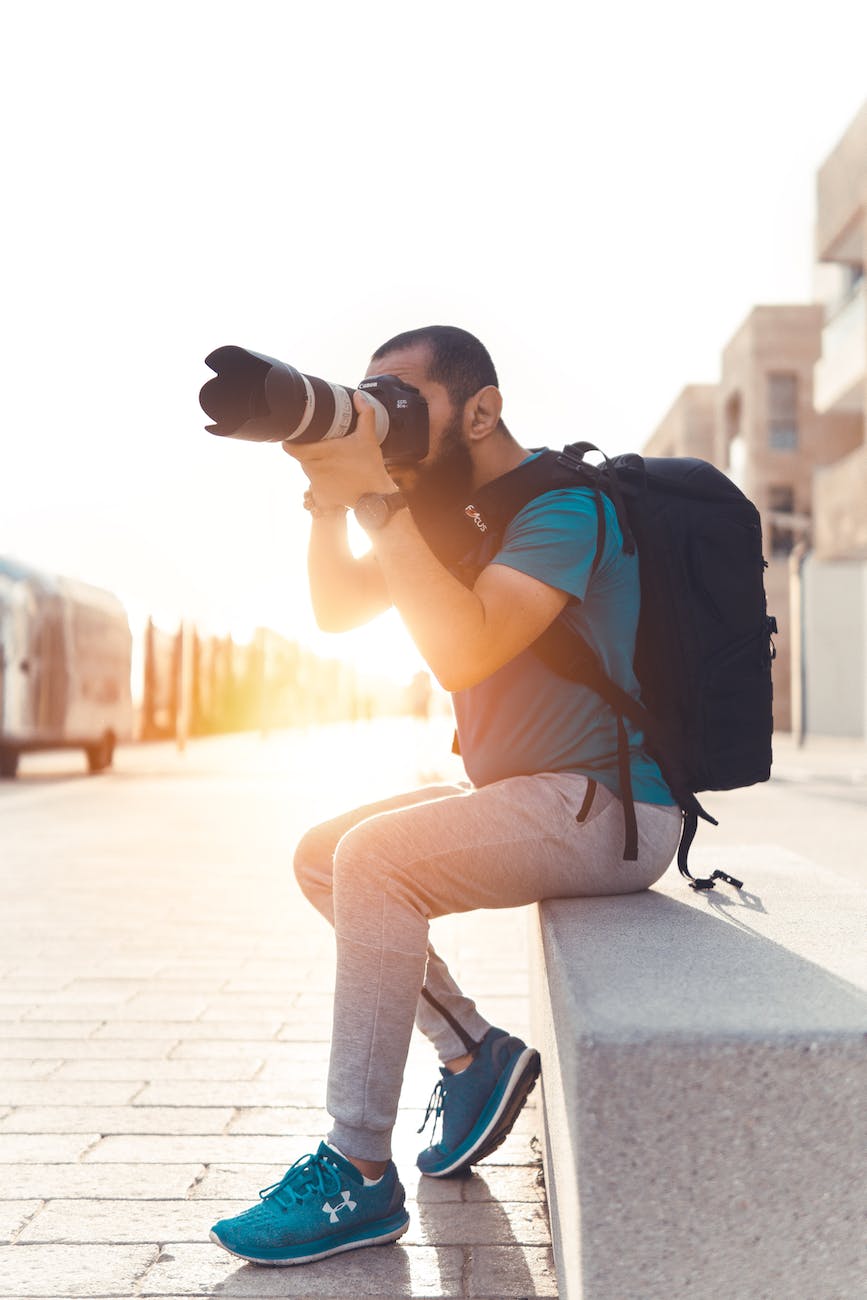 man carrying backpack taking photo using dslr camera