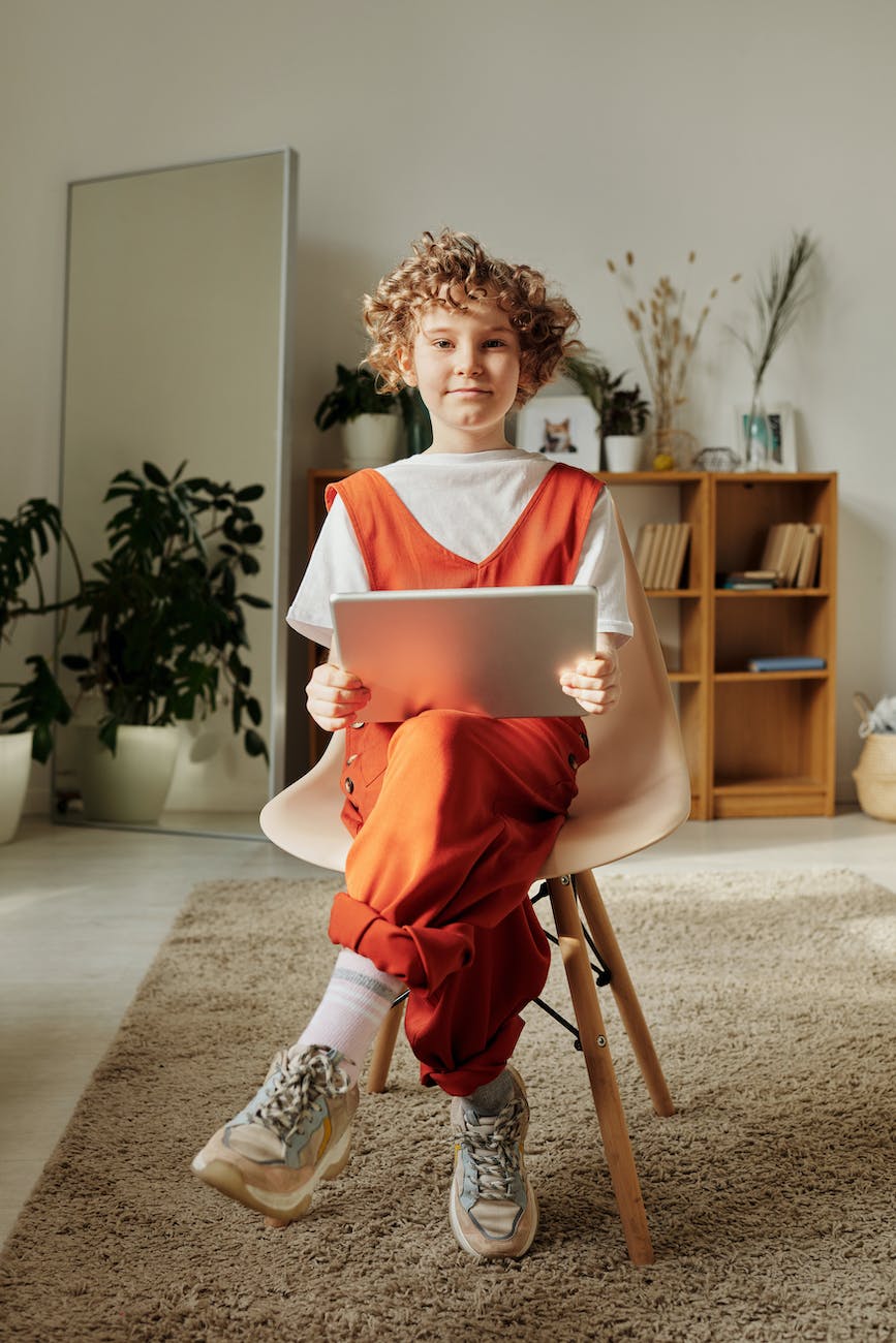 photo of child sitting on chair while using tablet